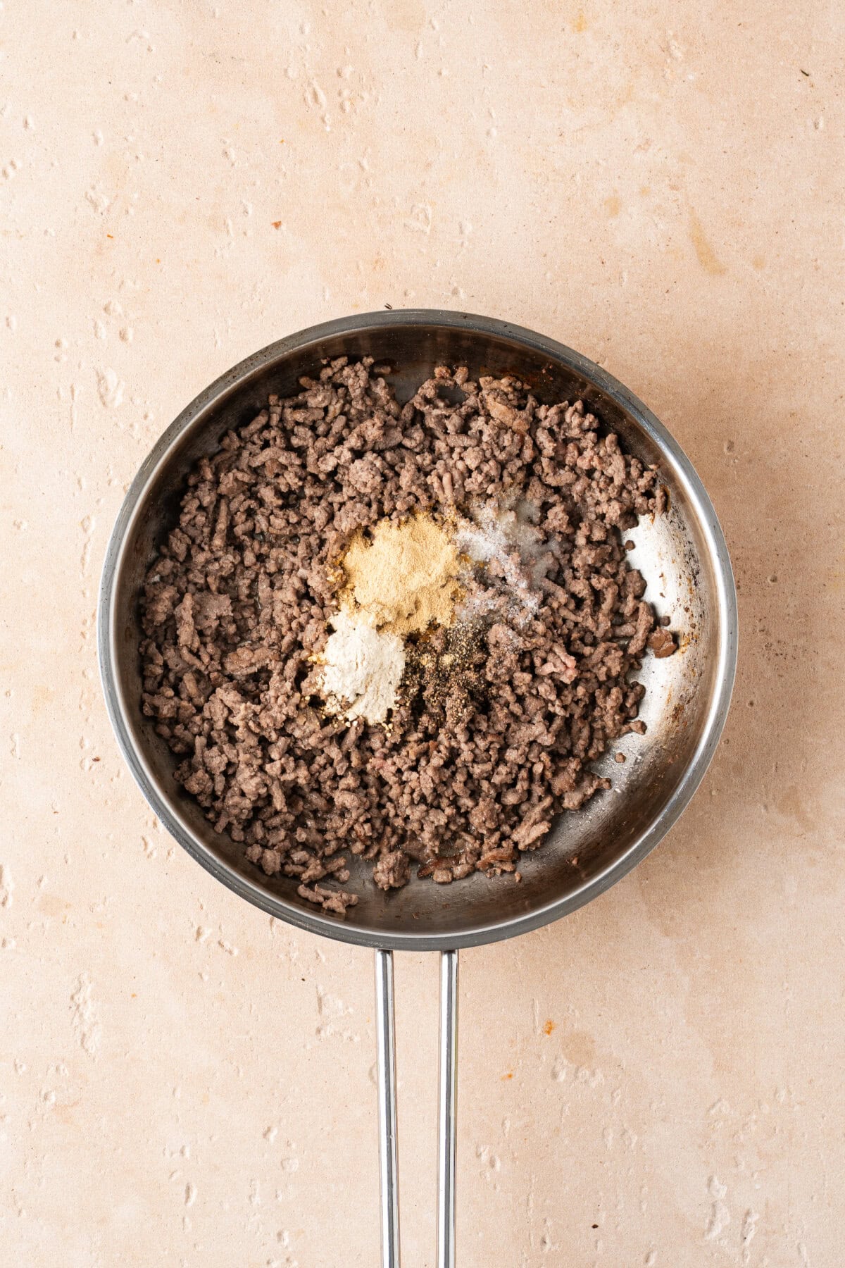 Salt, pepper, garlic powder, and onion powder sprinkled on top of cooked ground beef.