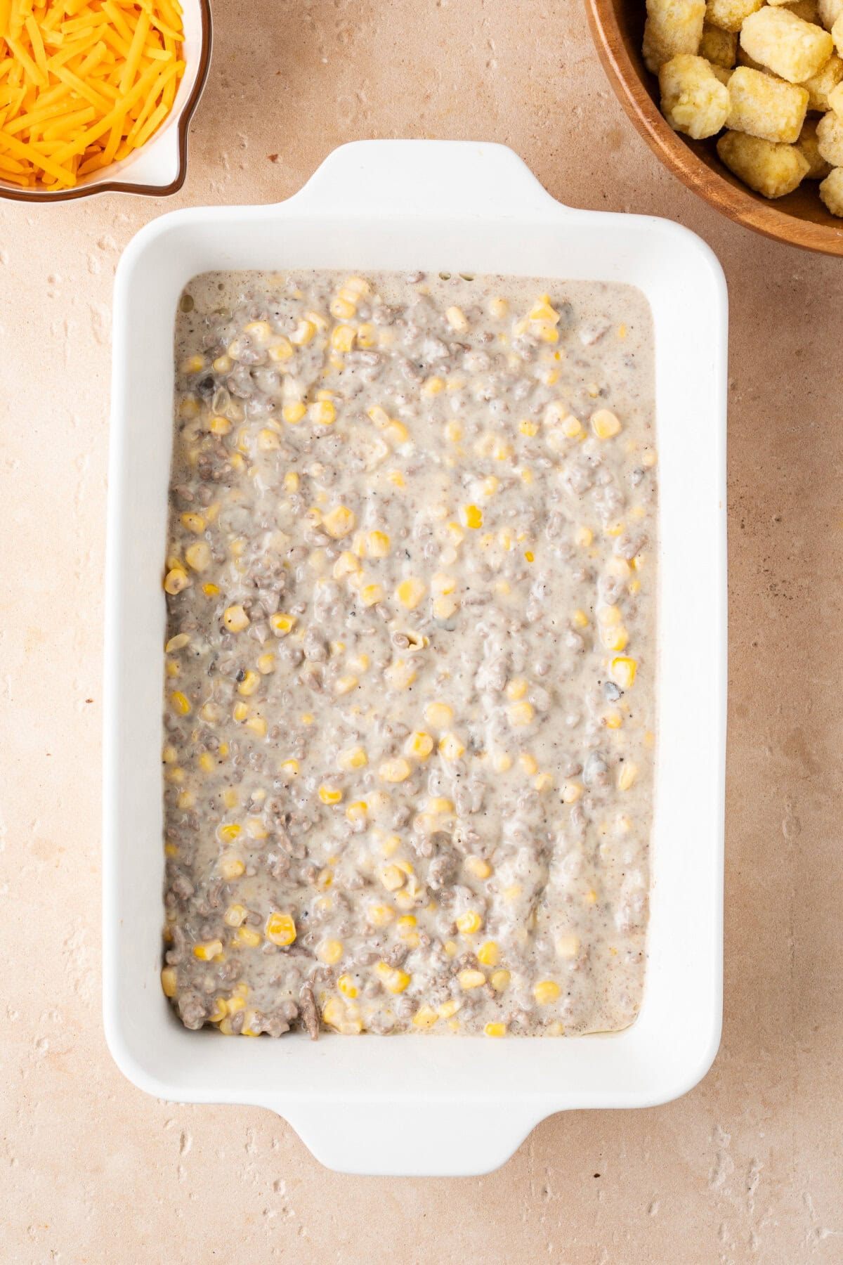 A ground beef and cream of mushroom mixture spread evenly onto the bottom of a prepared 9x13 baking pan.