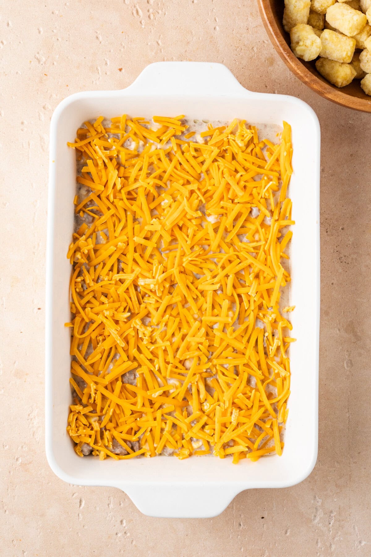 Shredded Cheddar cheese sprinkled on top of a ground beef mixture in a baking dish.