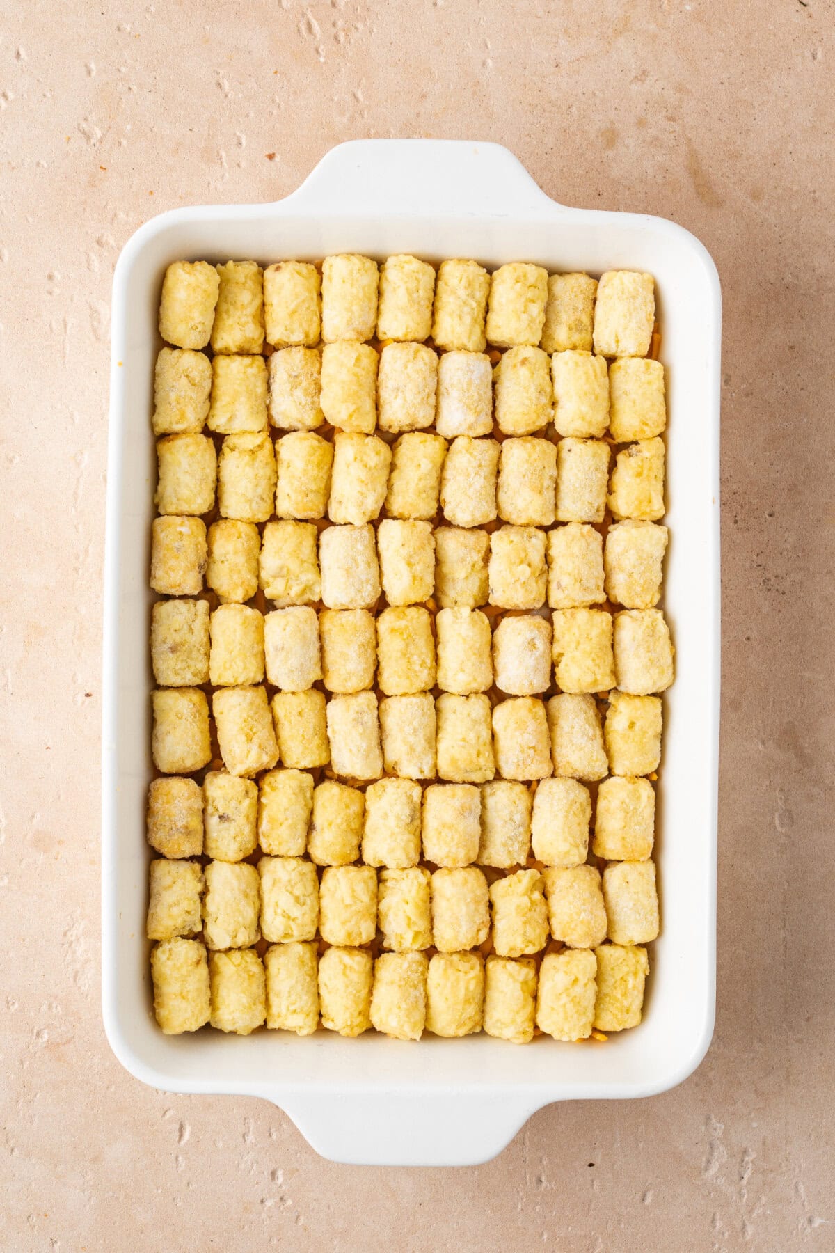 Tater tots lined up evenly over a ground beef mixture in a baking dish.