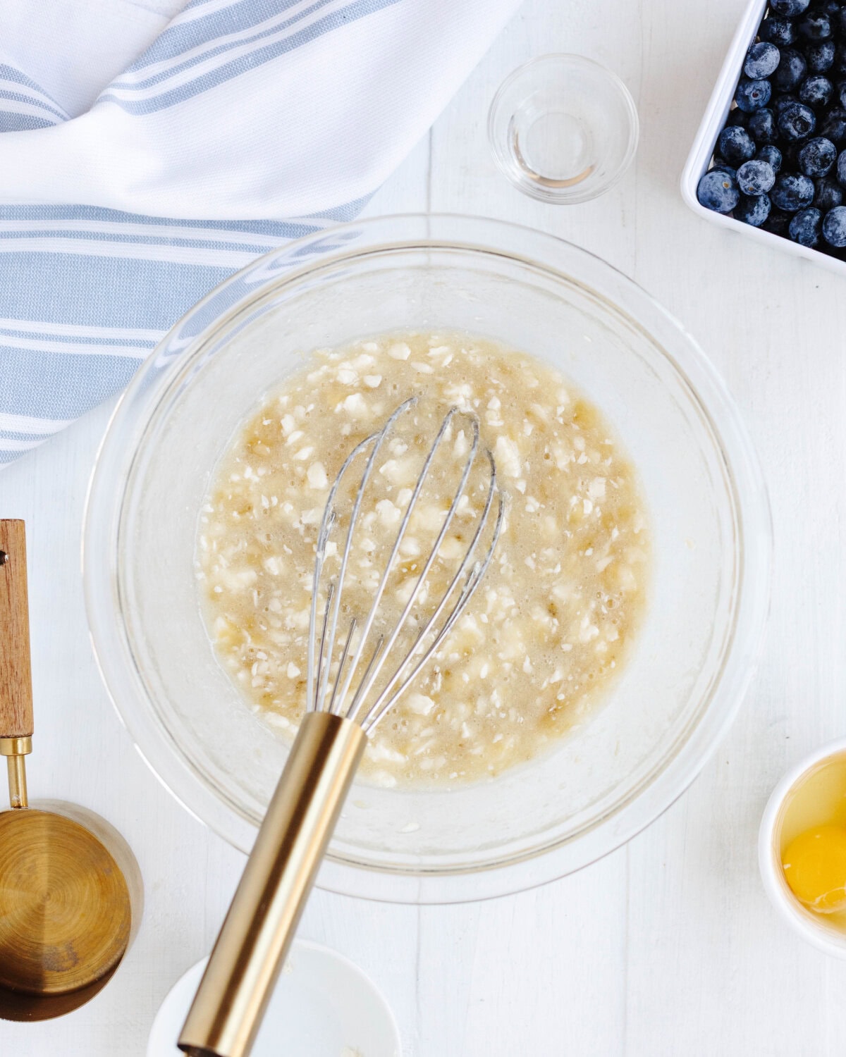 Softened butter and sugar added to mashed bananas in a glass mixing bowl.