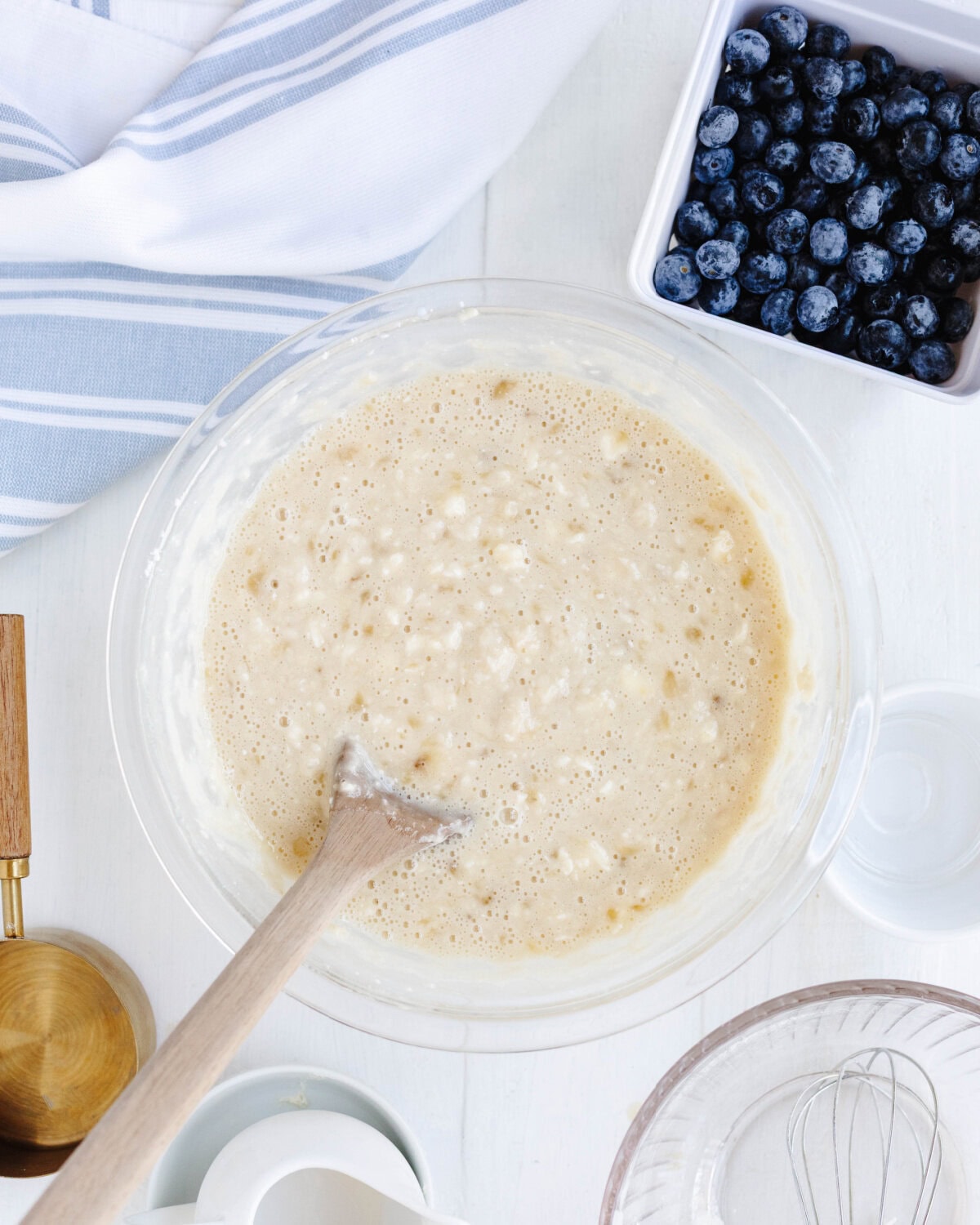 Eggs, vanilla, and milk added to a mashed banana mixture in a glass mixing bowl.
