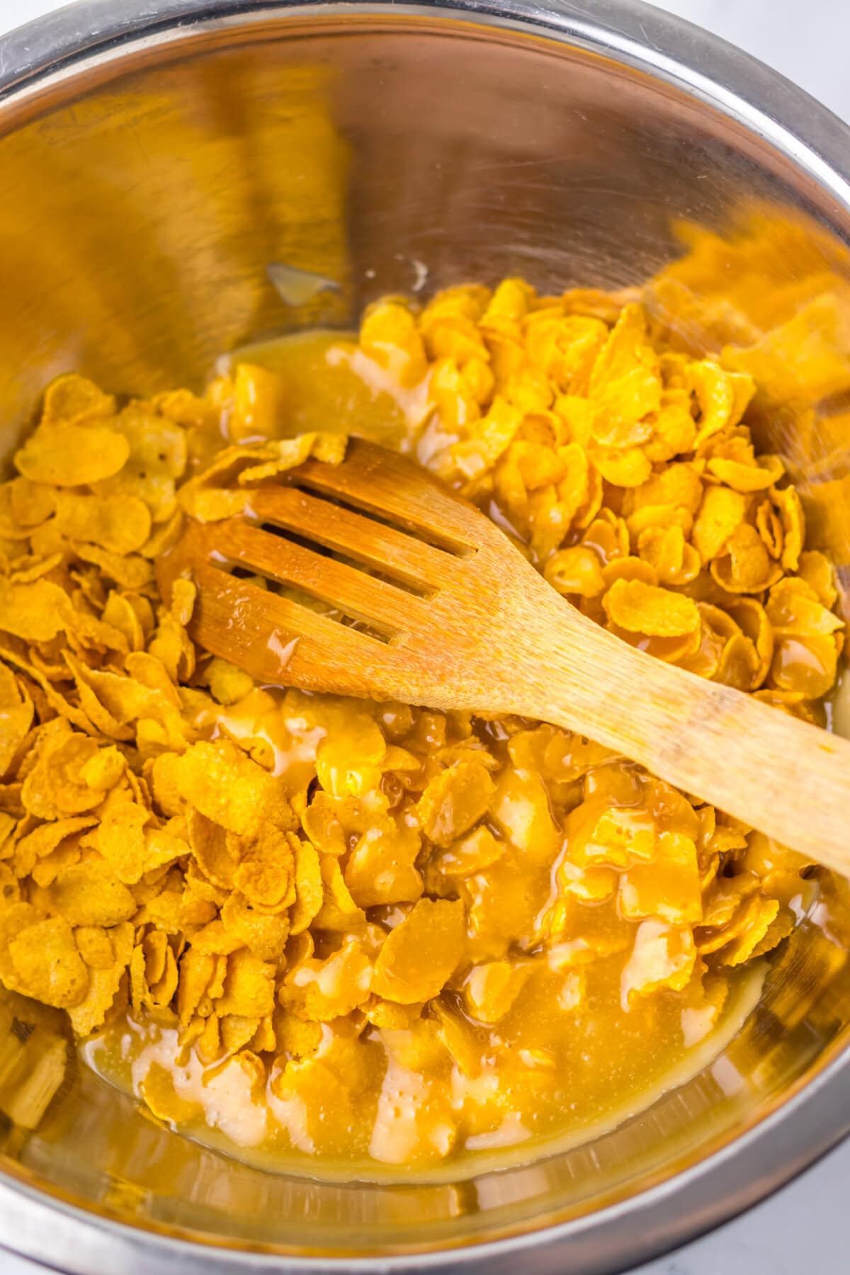 Cornflakes stirred into a brown sugar mixture in a mixing bowl.