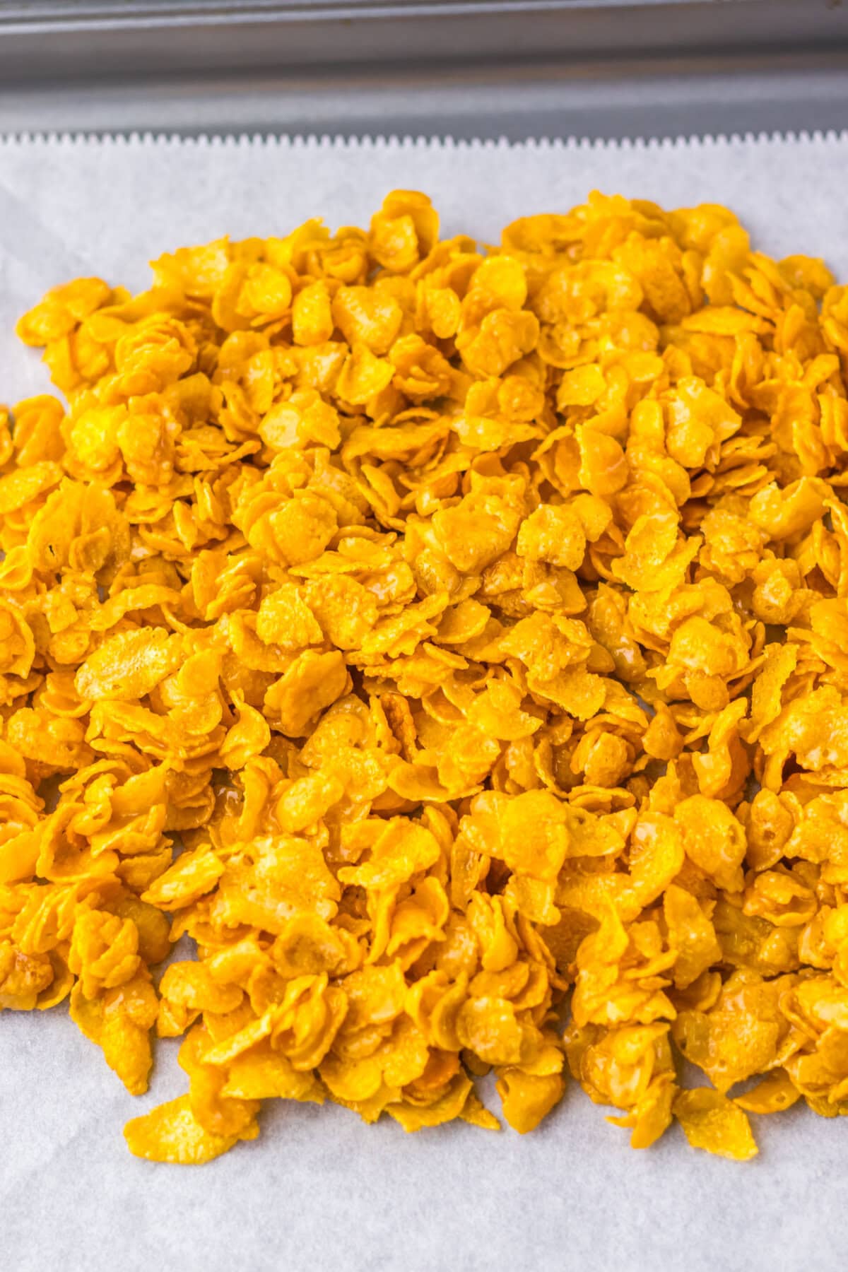Coated cornflakes spread in an even layer on a parchment paper lined cookie sheet.