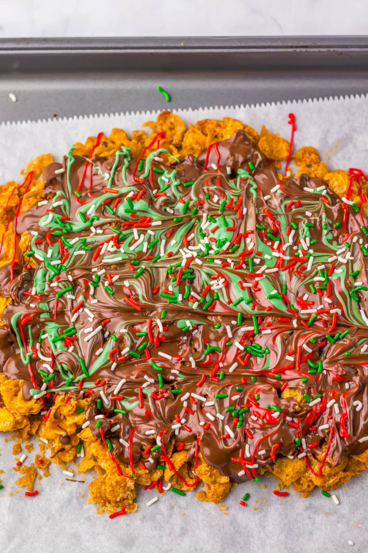 Almond bark and candy melts coating a brown sugar cornflake mixture on a parchment lined cookie sheet.