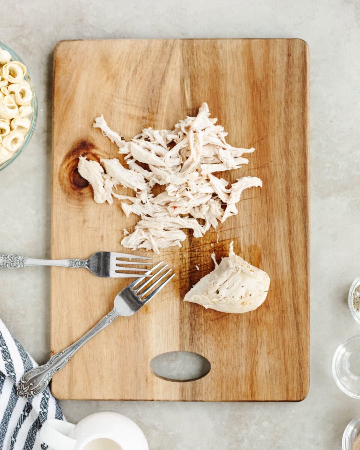 Cooked chicken removed and shredded on a wood cutting board.