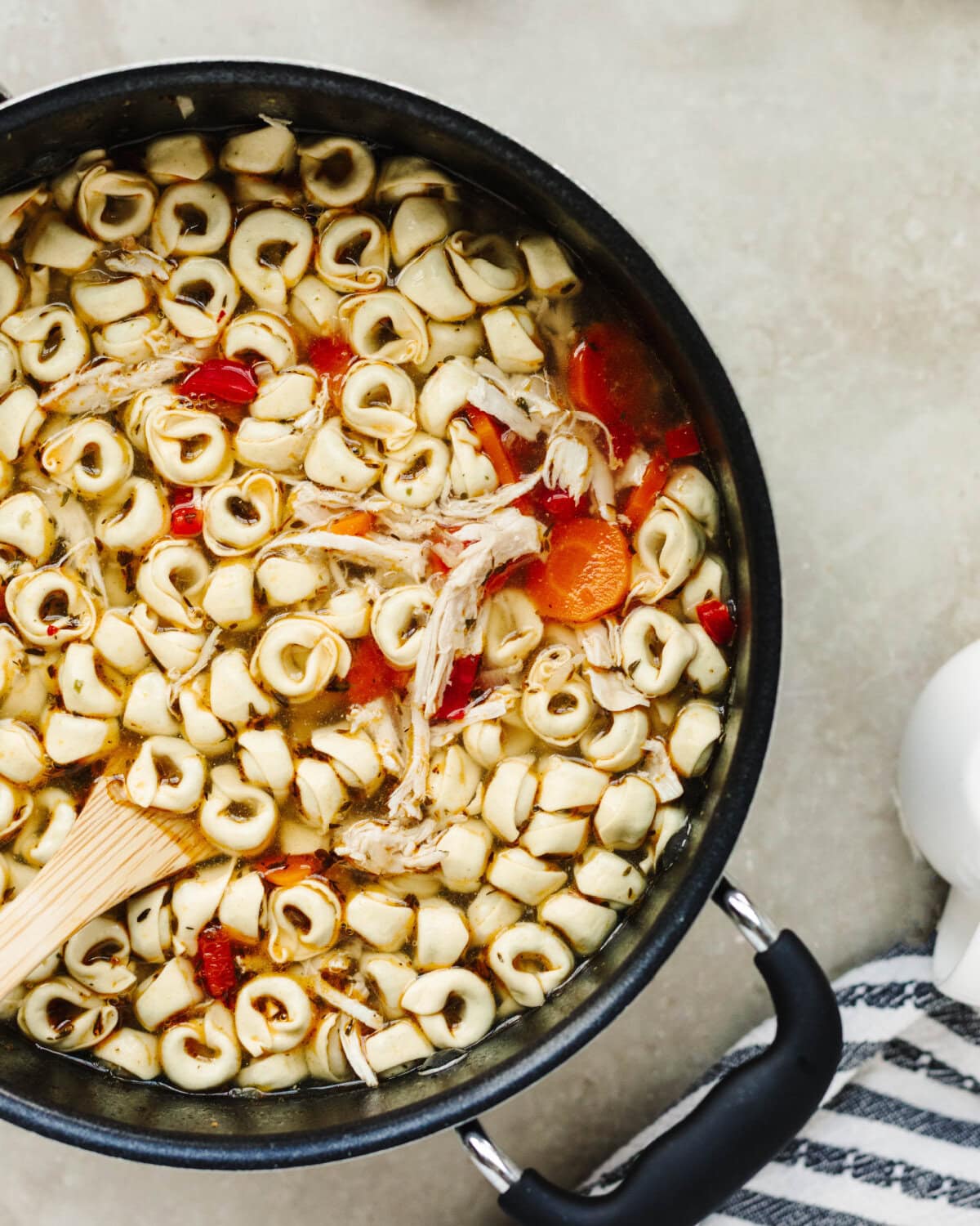 Cheese tortellini stirred into a chicken broth mixture in a soup pot.