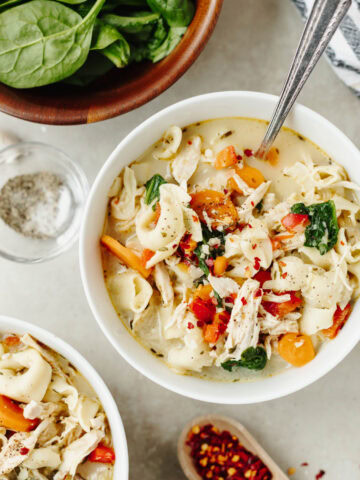 A white bowl with creamy chicken tortellini soup served with a spoon.