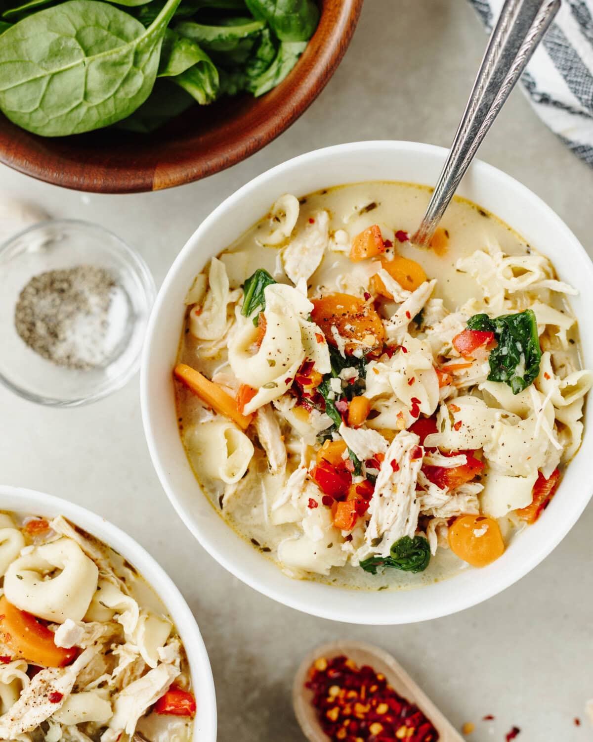 A white bowl with creamy chicken tortellini soup served with a spoon.