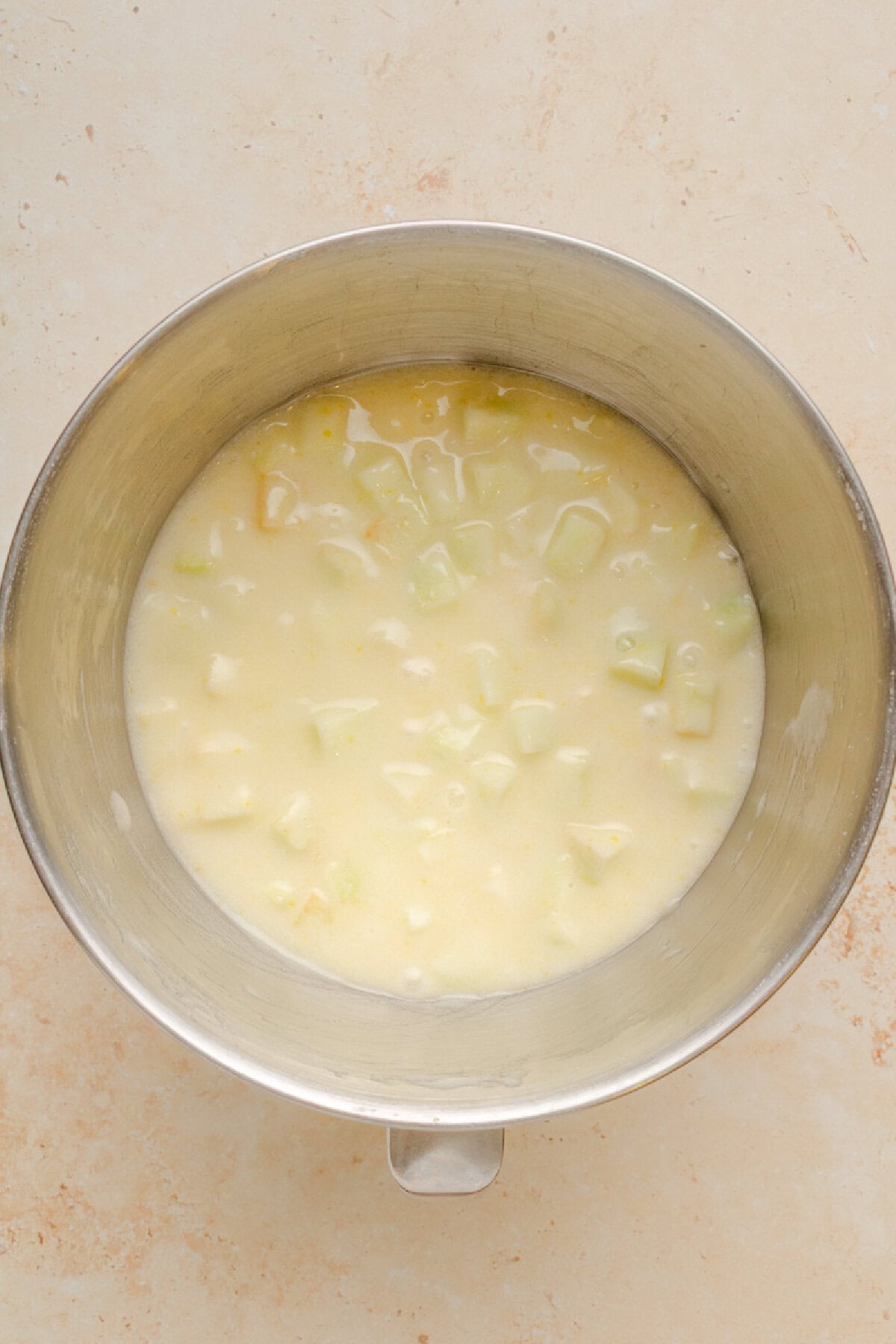Sugar, oil, eggs, and apples combined in a mixing bowl.