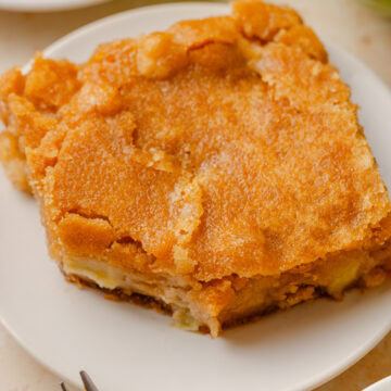 A slice of fresh apple cake on a white serving plate.