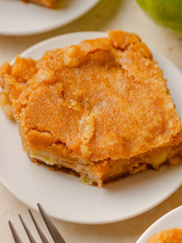 A slice of fresh apple cake on a white serving plate.