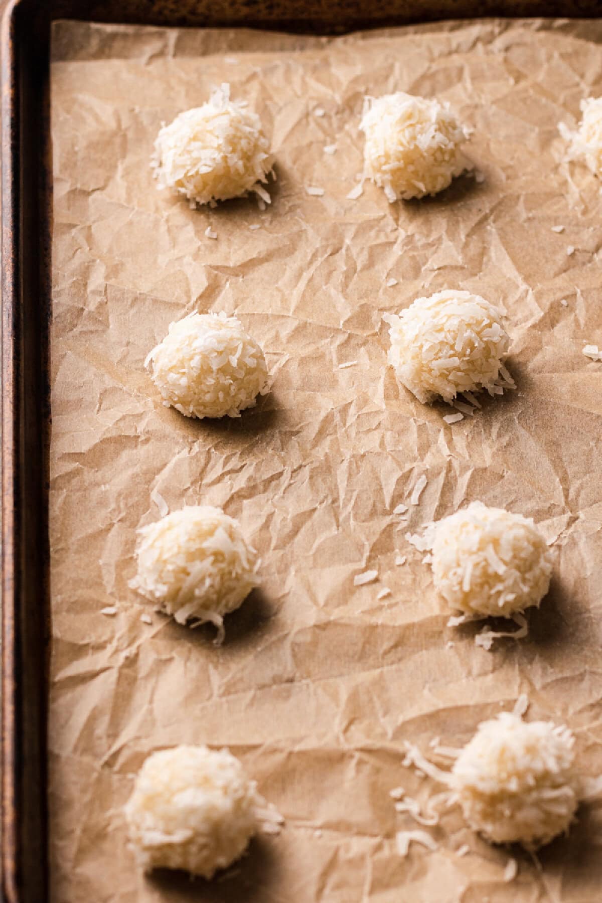 Coconut coated cookie dough balls placed on a parchment lined cookie sheet.