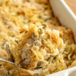 A spoon scooping up a serving of tuna casserole from a white baking pan.