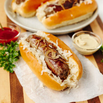 A bratwurst served in a bun with onions and seasonings and served on a wood cutting board.