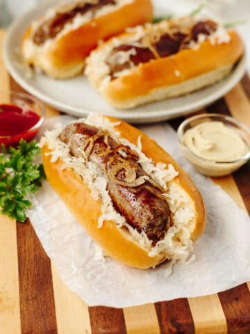 A bratwurst served in a bun with onions and seasonings and served on a wood cutting board.