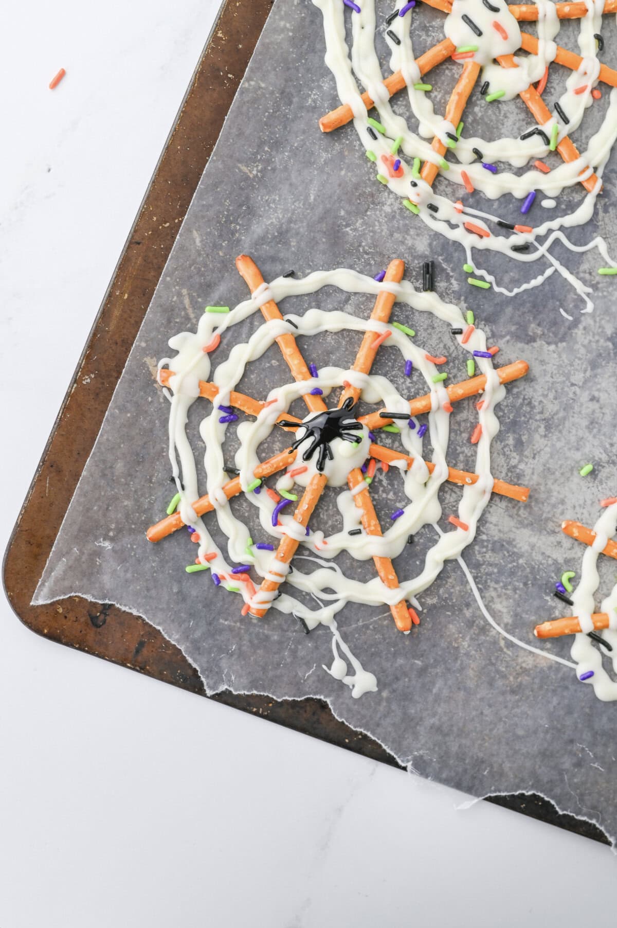 A parchment lined cookie tray with pretzels forming spider webs for Halloween.