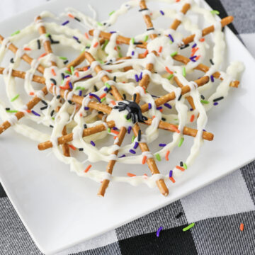 A black icing spider on top of a spider web chocolate pretzel stack on a white plate.