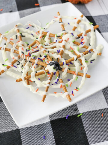 A black icing spider on top of a spider web chocolate pretzel stack on a white plate.