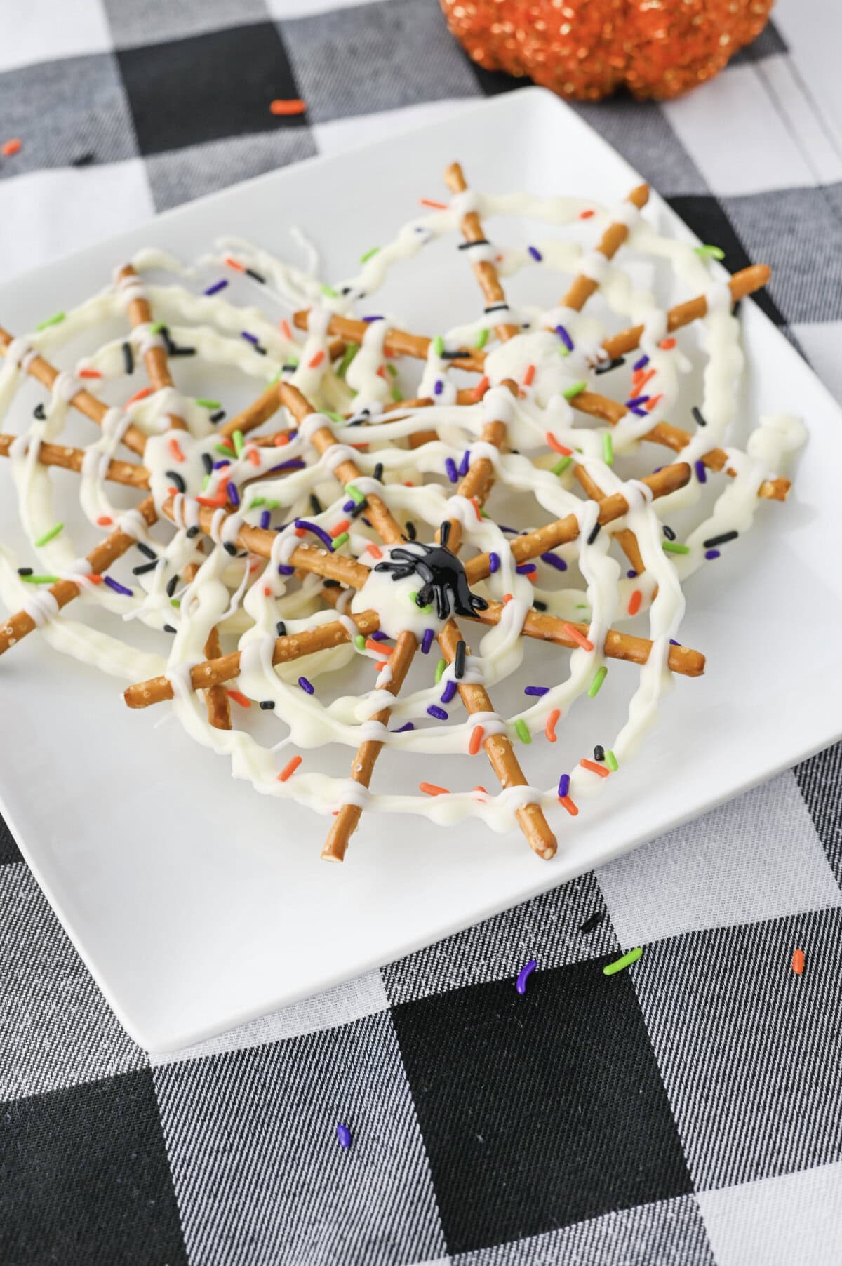 A black icing spider on top of a spider web chocolate pretzel stack on a white plate.