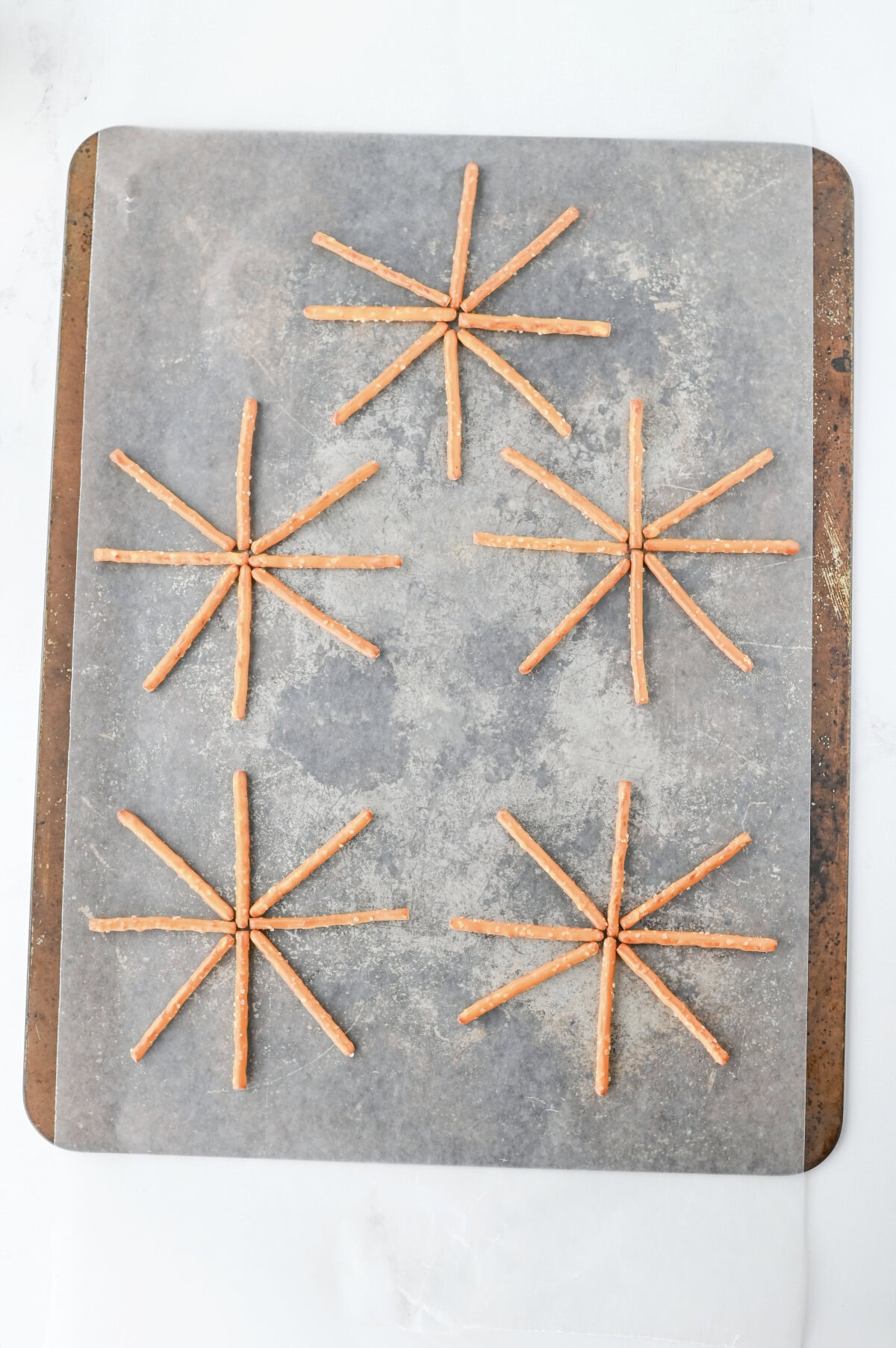 Pretzel sticks aligned into circles on a parchment lined cookie sheet.
