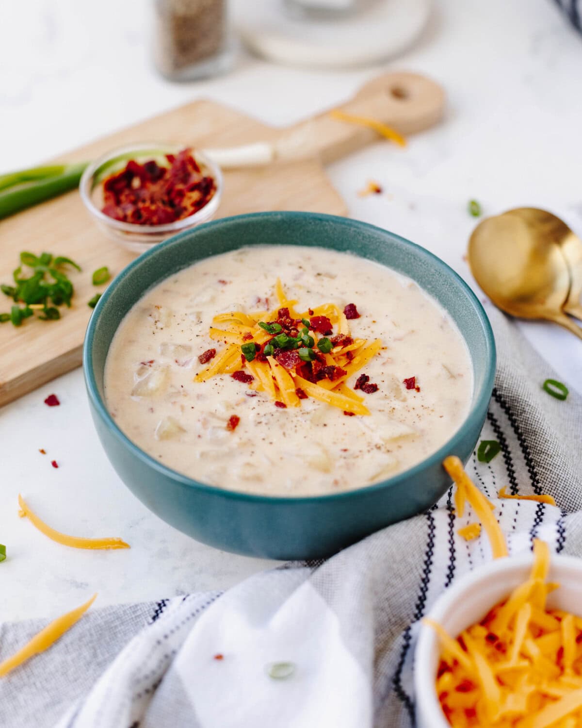 A blue bowl with loaded baked potato soup topped with shredded cheddar cheese, bacon, and chives.