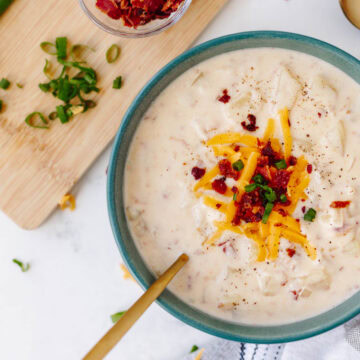 A top view of a bowl of ultimate potato soup topped with bacon, cheese, and green onions.