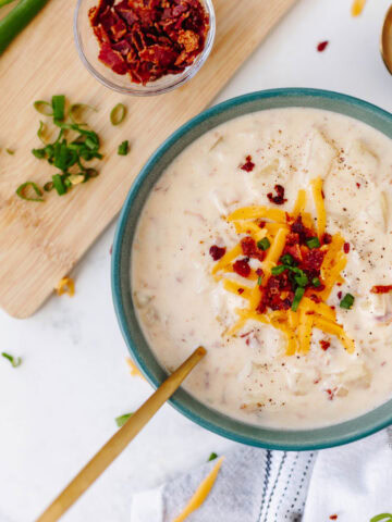 A top view of a bowl of ultimate potato soup topped with bacon, cheese, and green onions.