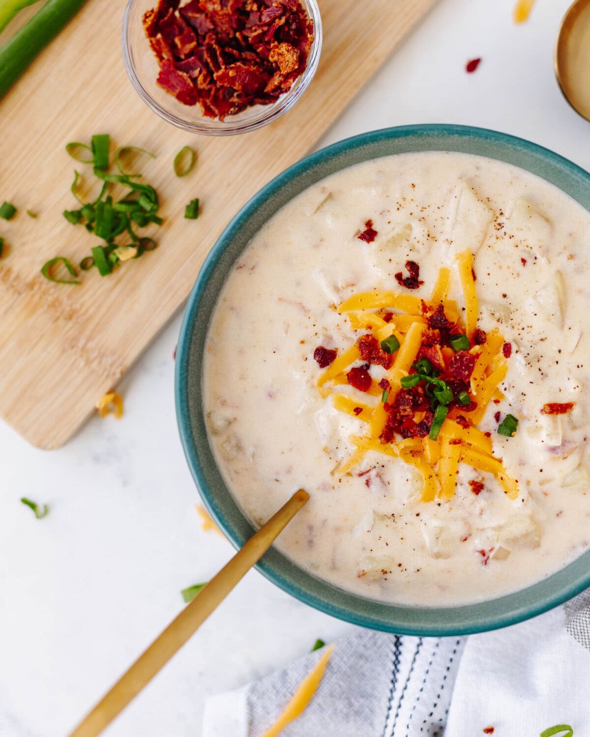 A top view of a bowl of ultimate potato soup topped with bacon, cheese, and green onions.