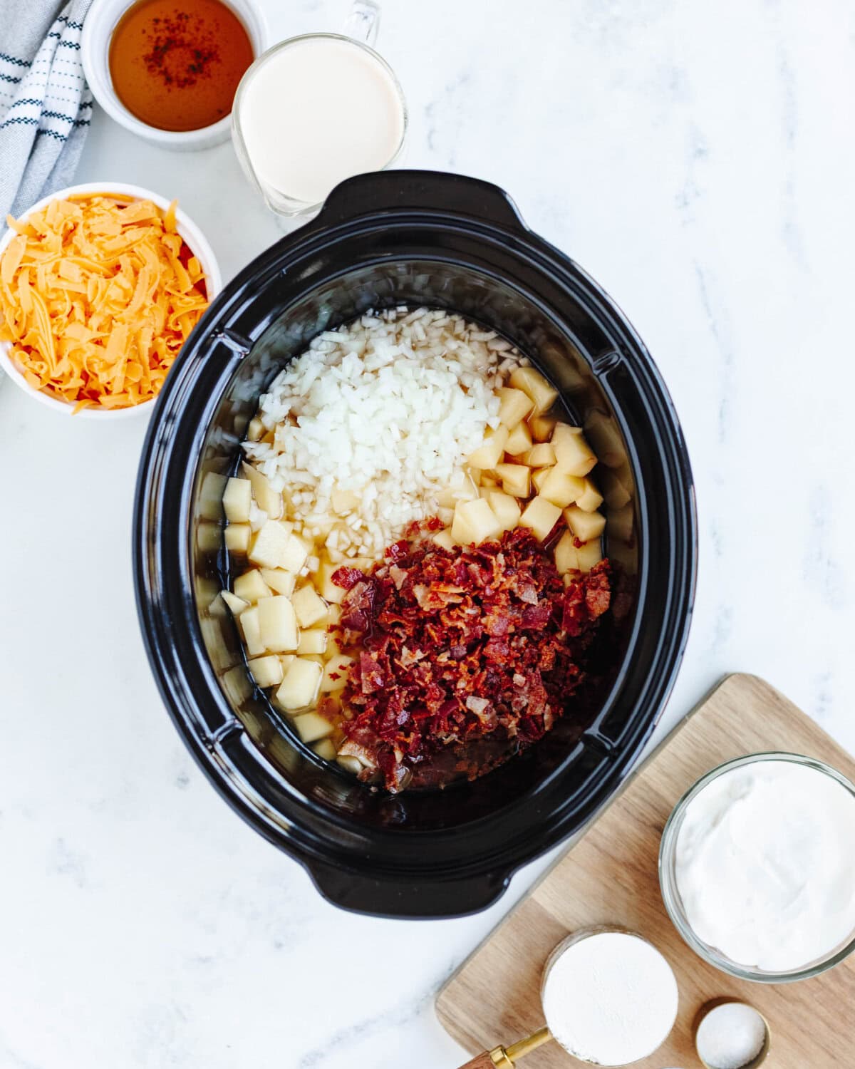 Bacon, chicken broth, potatoes, and onions added to a slow cooker.